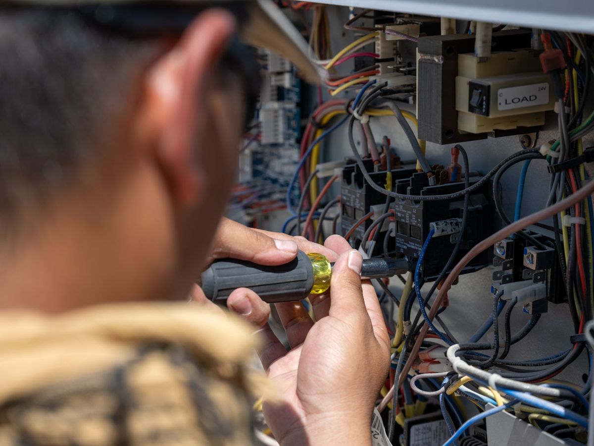 Technician testing wiring inside an HVAC control panel