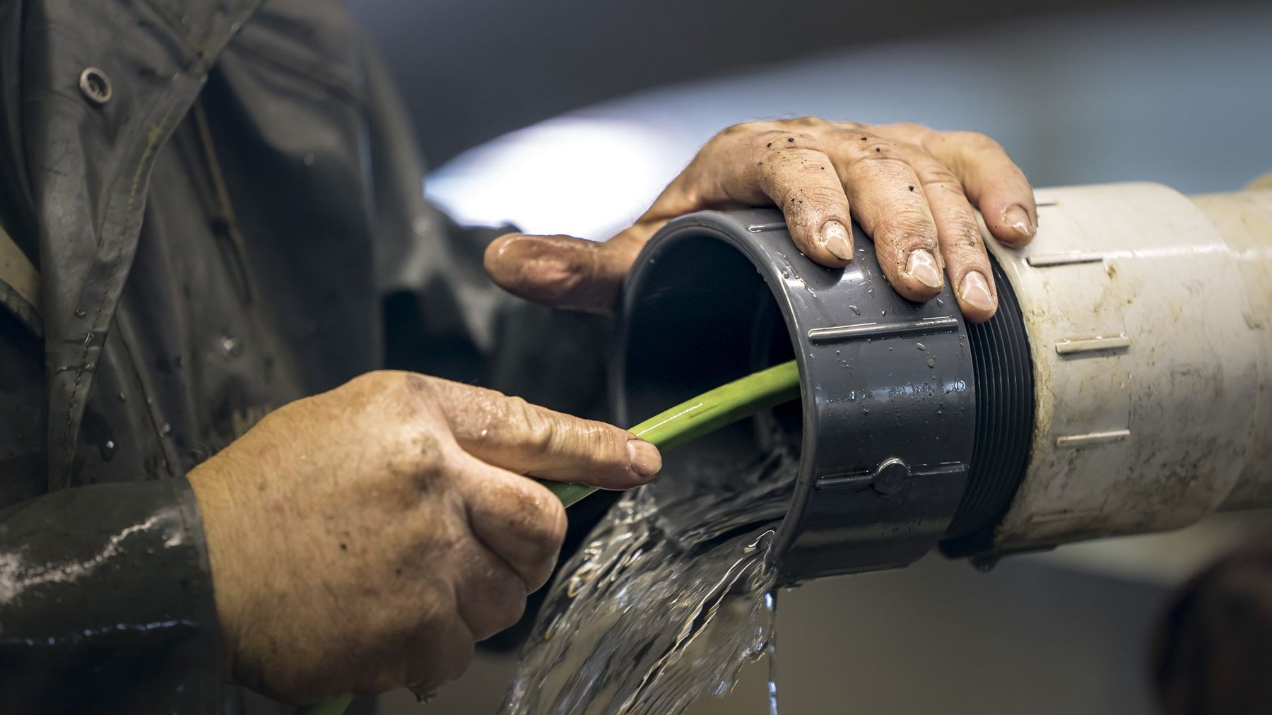 Plumber's hands on a pipe fitting with water flowing out
