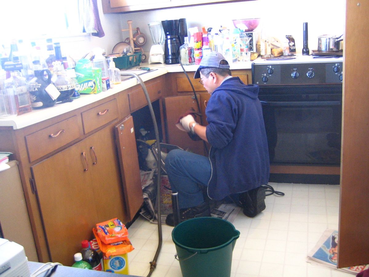 Plumber repairing pipes under a kitchen cabinet